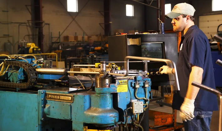 Operator loading a tube into a bending machine on a shop floor